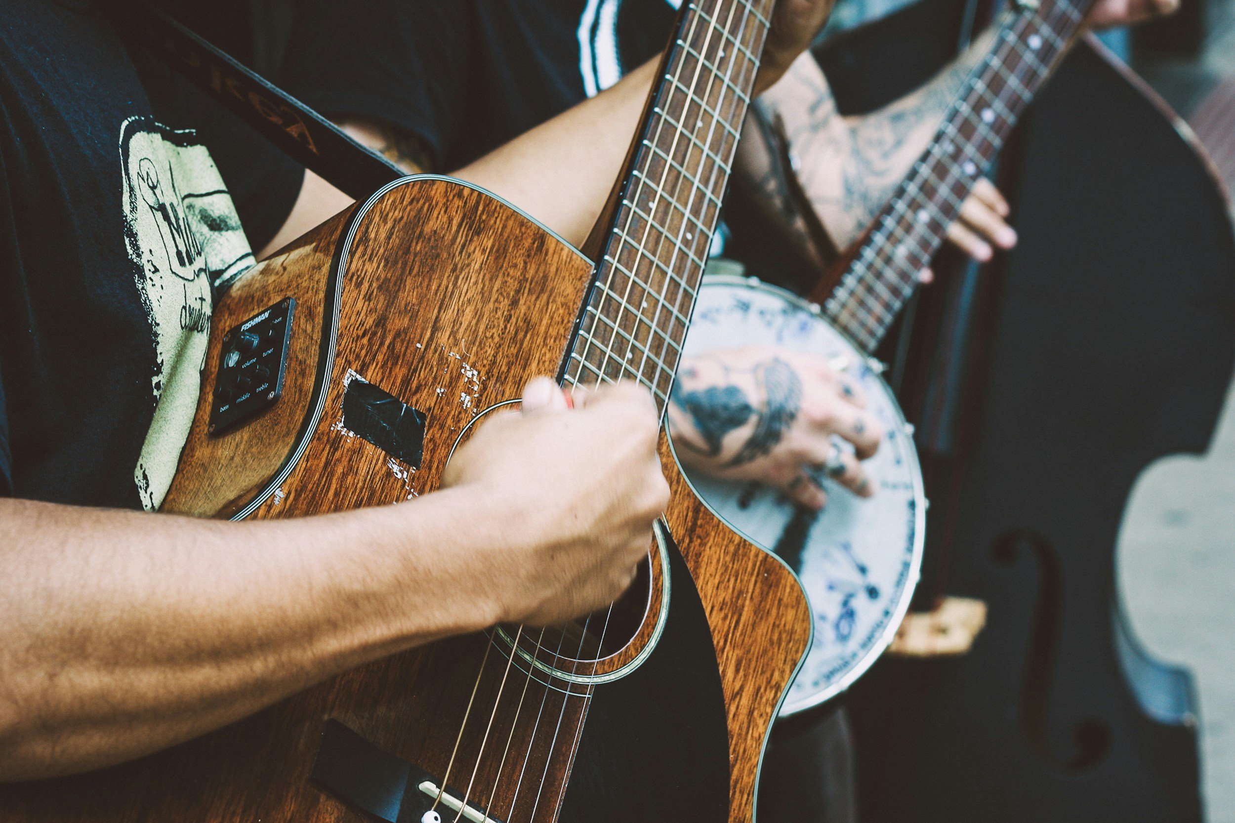 Two musicians play an electric acoustic guitar and a banjo. Another musician plays the cello in the background.