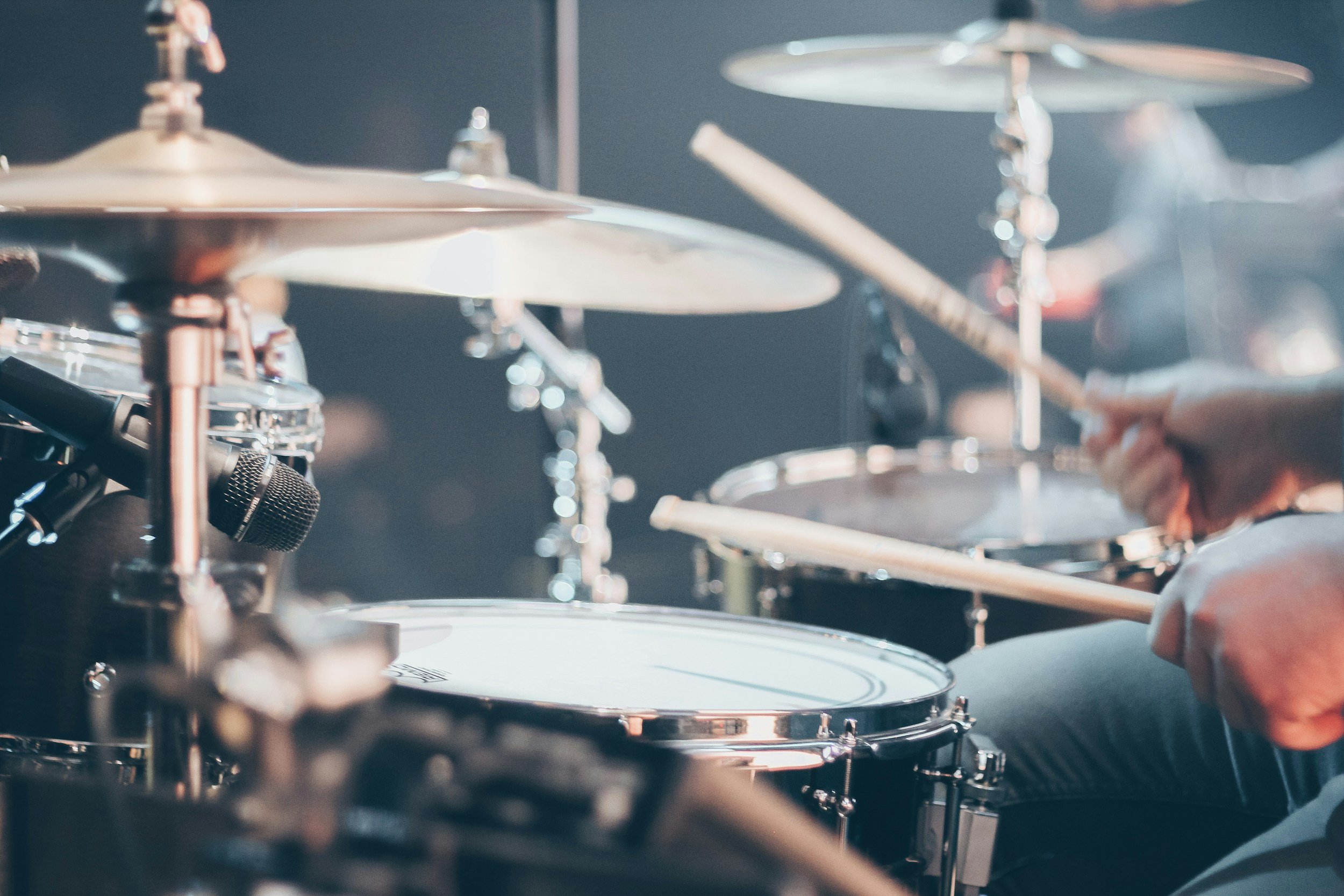 To the right, hands holding drumsticks hover above a drum set, about to strike.
