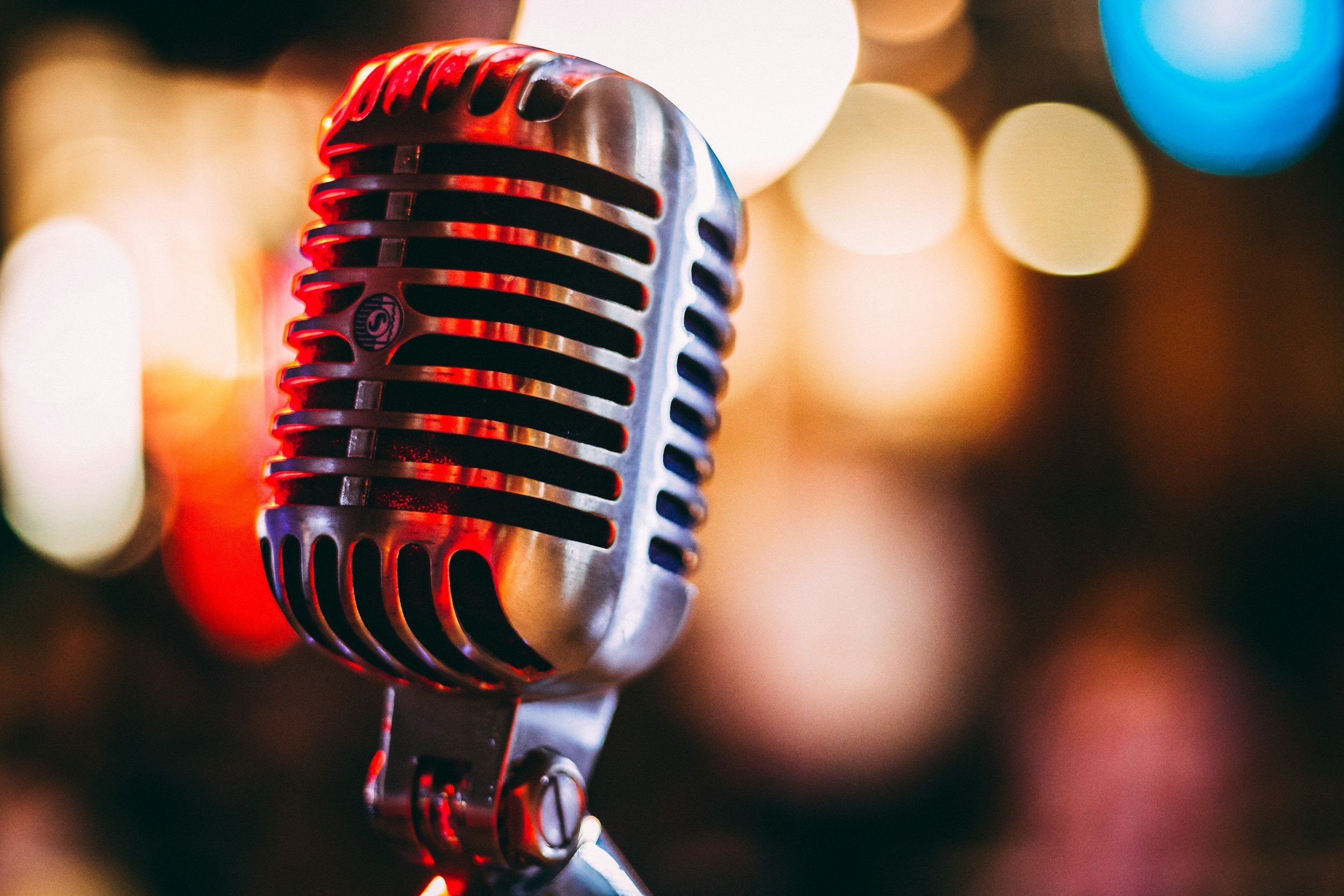 A close up photo of a vintage microphone, with blurred lights in the background.